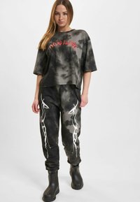Černošedé tričko s krátkým rukávem tie-dye s nápisem "Drive Life" v červené barvě; odpovídající teplákové kalhoty s bílým abstraktním vzorem; doplněno černými botami.