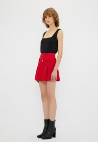 Top negro sin mangas, falda corta acampanada roja con un cinturón que acentúa la cintura, y botas de tacón negras hasta el tobillo. Tela suave y ajuste entallado.