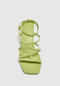 Sandal in plastica verde con cinturini incrociati, design a punta quadrata, tacco piatto e superficie liscia. Dettagli hardware minimi.
