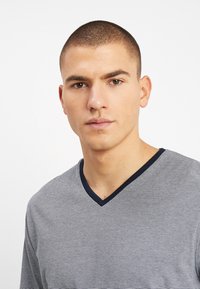 T-shirt a maniche corte a V in blu e bianco a righe con colletto blu navy, caratterizzato da una morbida texture e una forma aderente.