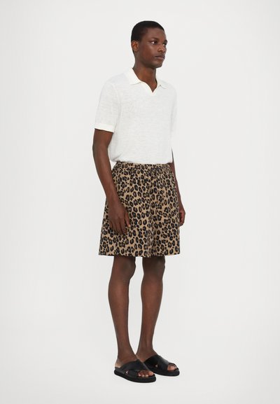 Short-sleeve, white polo shirt with a pale collar, paired with knee-length, beige shorts featuring a black leopard print, worn with black slides.