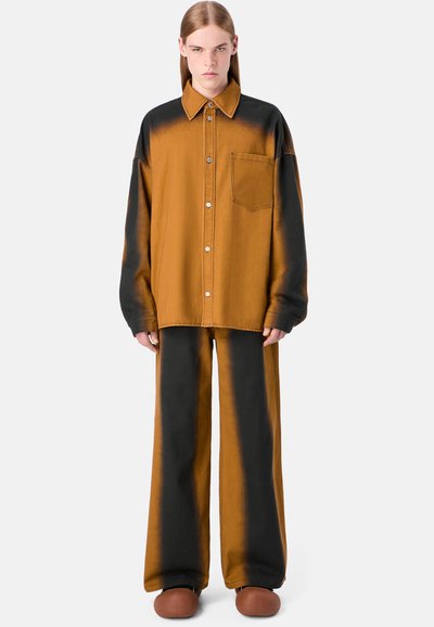 Camicia oversize a gradient arancione bruciato e nero con colletto, bottoni e taschino frontale, abbinata a pantaloni larghi coordinati e scarpe marroni.