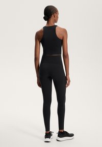 Top corto sportivo nero e leggings a vita alta realizzati in materiale elastico, con una texture liscia e un design aderente.
