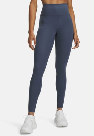 Marineblauwe high-waisted leggings gemaakt van een glad, rekbaar materiaal, met een strak ontwerp en zijzakken, gecombineerd met witte sportschoenen.