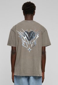 Grå bomulls T-skjorte med korte ermer, med et dristig svart og blått grafisk design på baksiden, inkludert skarpe linjer og en hjerteform.
