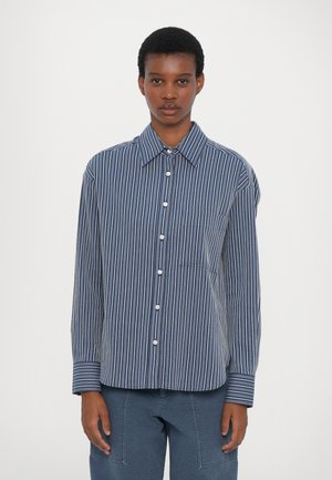 Chemise à boutons navy avec des rayures verticales blanches, dotée d'un col classique, de manches longues et d'une poche sur le devant. Texture de tissu douce.