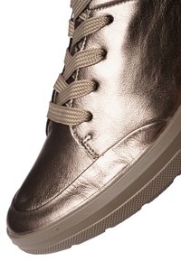 Close-up van een metalen bronzen sneaker met gestructureerde beige veters en dikke rubberen zool, met zicht op de bovenkant en zijkant.