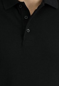 Polo negro hecho de tejido texturizado con un collar y tres botones negros. Diseño minimalista sin logotipos ni patrones visibles.