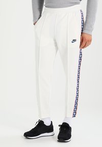 Vita Nike-joggers med sidosträck i ett geometriskt mönster i röd, blå och svart. Slät tyg, tapered design, elastisk midja.
