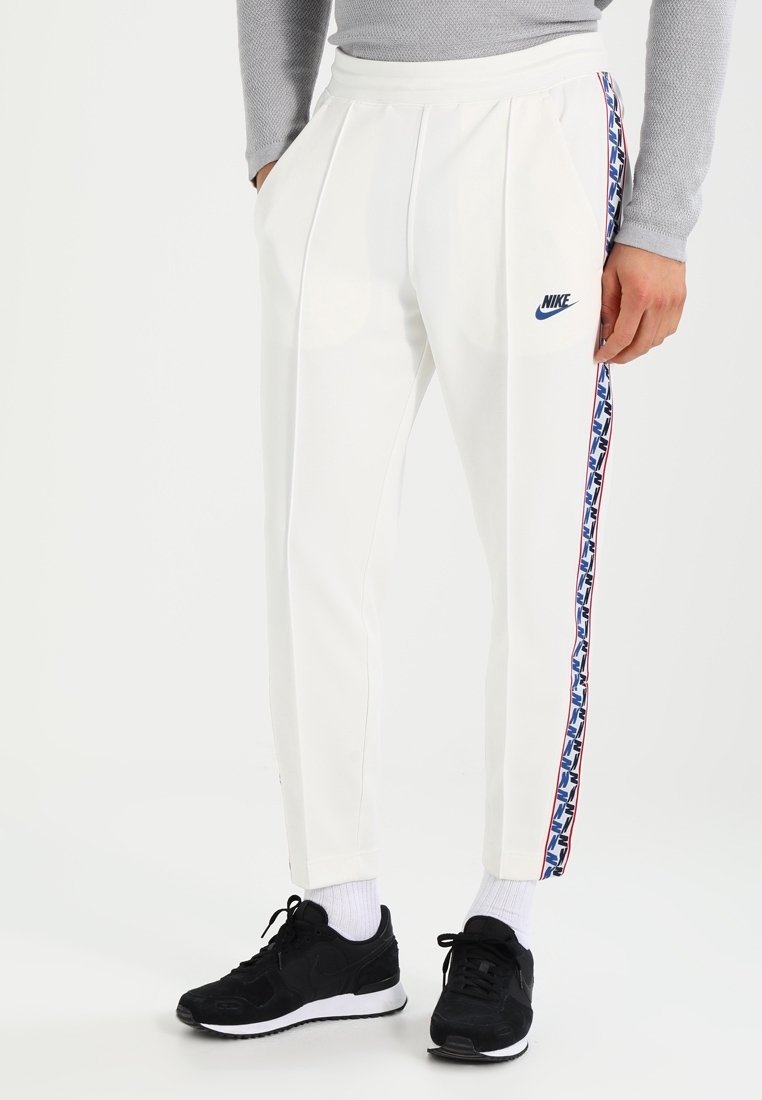 Vita Nike-joggers med sidosträck i ett geometriskt mönster i röd, blå och svart. Slät tyg, tapered design, elastisk midja.