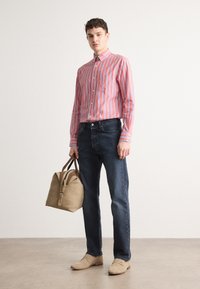 Camisa a rayas en rojo y azul, jeans oscuros, bolso beige y zapatos claros. La camisa presenta un cuello abotonado y mangas alargadas.