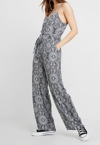 Combinaison à motifs noir et blanc avec un corsage ajusté, des jambes larges et des bretelles réglables ; dotée d'une ceinture à nouer et de poches latérales.