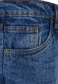 Blauwe denim spijkerbroek met een achterzak met oranje stiksels en een kleine metalen klinknagel. De stof heeft een subtiele textuur en slijtage.
