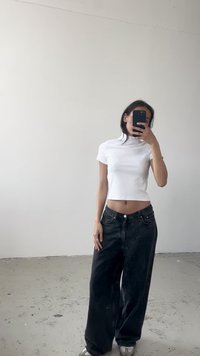 Vitt, figurnära, kortärmad croptop i kombination med lösa, svarta, högmidjade jeans. Har en hög krage och en avslappnad silhuett.