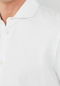 White polo shirt with a textured fabric, featuring a small embroidered logo on the chest and a three-button placket.