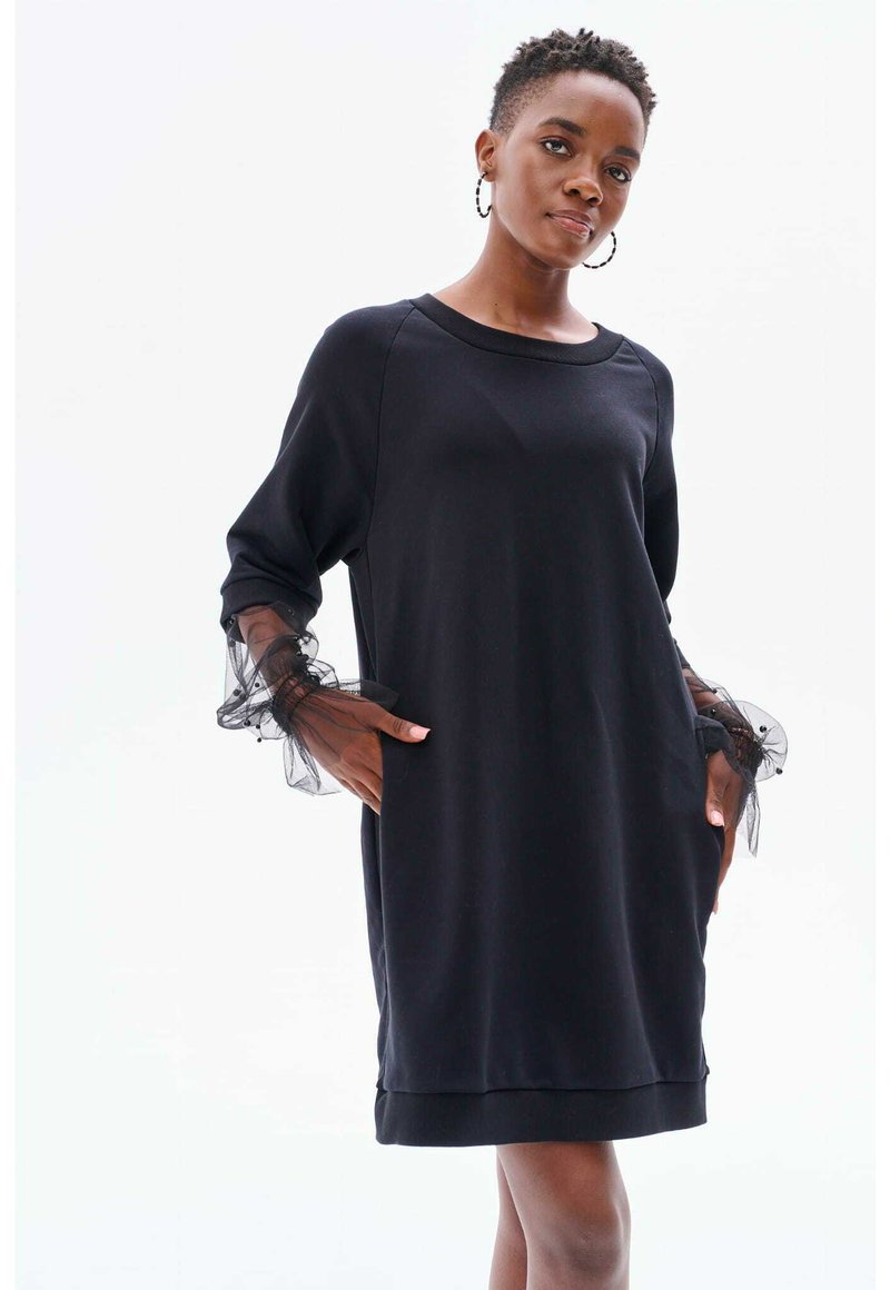 Schwarzes Kleid aus weichem Stoff mit langen Ärmeln, das Tüllakzente aufweist. Das Design hat einen runden Ausschnitt und seitliche Taschen. Einfarbig.