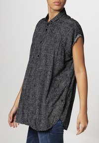 Chemise à manches courtes à motifs noir et blanc avec un col, présentant une coupe décontractée et un ourlet arrondi.