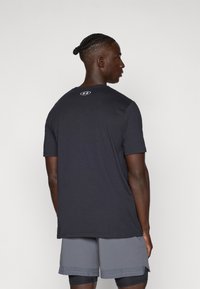 Kortärmad, mörkgrå sportt-shirt med rund halsringning och liten logotyp på baksidan. Tyget ser jämnt och lätt ut.