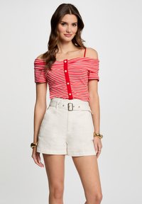 Top de tirantes caídos a rayas rojas y blancas con mangas cortas y detalle de botón en el centro, combinado con pantalones cortos blancos de tiro alto con cinturón.