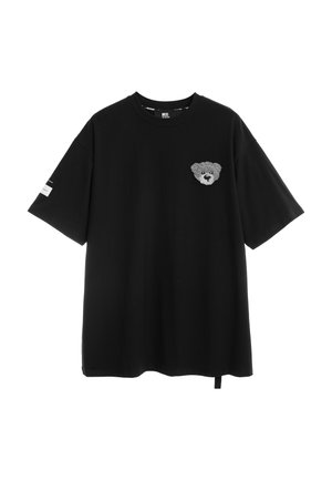 Camiseta negra de manga corta con cuello redondo y una pequeña cara de oso de peluche gris bordada en el pecho izquierdo.