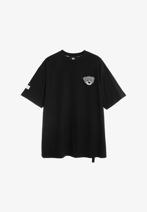 Camiseta negra de manga corta con cuello redondo y una pequeña cara de oso de peluche gris bordada en el pecho izquierdo.