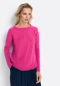 Fuchsia Langarmtop mit abgerundetem Saum und Rundhals-Ausschnitt, ausgestattet mit einer weichen Textur und einem lockeren Schnitt. Kombiniert mit navyblauen Hosen.
