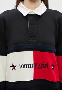 Čierny a biely dlhý rukáv polo tričko s farebnými pruhmi v červenej a smotanovej farbe, vyšitý nápis "tommy girl" a kontrastný golier.