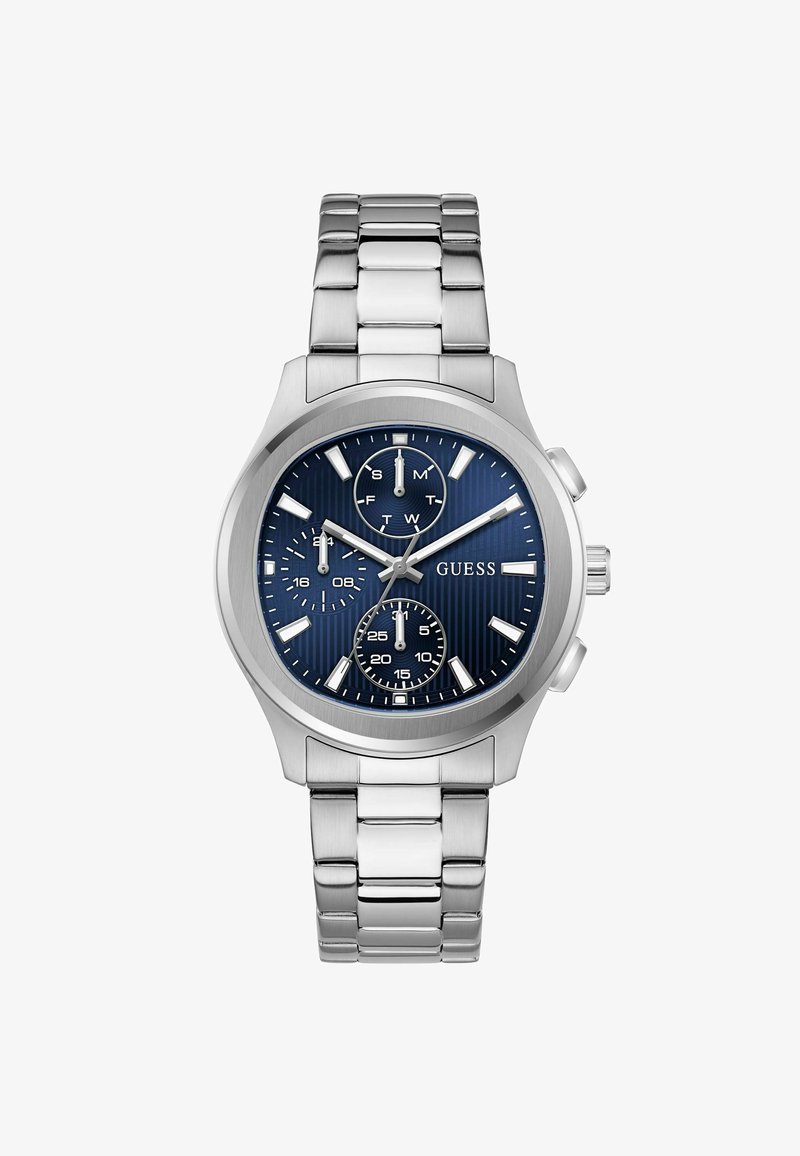 Montre-bracelet en métal argenté avec cadran bleu, trois sous-cadrans indiquant le jour, l'heure sur 24 heures et les secondes, et logo "GUESS" sur le cadran.