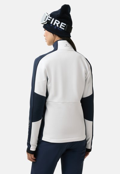 Weiß-navyblauer Reißverschluss-Jacke mit hohem Kragen, mit Farbblock-Design und Logo-Akzenten, kombiniert mit einer navyblauen Mütze und einer Schutzbrille.