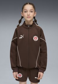 Conjunto deportivo marrón de chaqueta y pantalones cortos con acentos en blanco, con cierre de cremallera en el frente, parche con logo y marca Puma en el pecho y en los pantalones cortos.