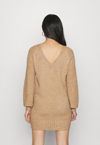 Strickkleid in hellem Beige, mit langen Ärmeln, einem tiefen V-Ausschnitt hinten, geripptem Saum und strukturiertem Stoff.