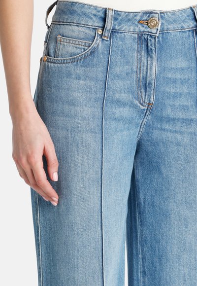 Svetlo modri jeans z visokim pasom, širokimi nogavicami in vidnimi sprednjimi žepi. Imajo rahlo pranje in kontrastne oranžne šive.