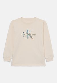 Dlhý rukáv svetločerveného trička vyrobeného z bavlny, s viacerými farebnými grafikami "CK" a textom "Calvin Klein Jeans" vpredu.