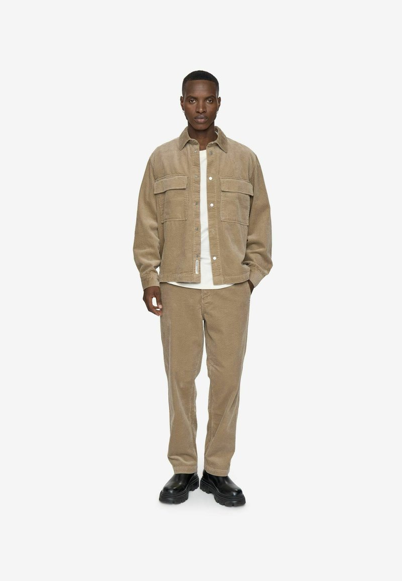 Beige corduroy jakke med to brystlommer, knaplukning, parret med matchende bukser og sorte sko. Enkel hvid skjorte under.