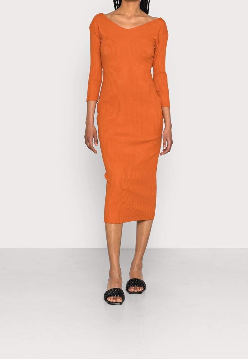 Robe midi orange à rayures avec décolleté en V et manches trois-quarts, associée à des sandales noires à enfiler tressées. Texture lisse, design ajusté.