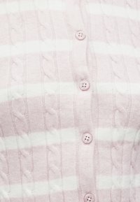 Gaiši rozā džemperis ar baltām svītrām. Ievērojama adījuma tekstūra un seši rozā pogas priekšpusē. Mīksts, adīts materiāls.