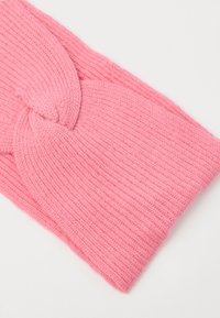 Fascia per la testa lavorata a maglia in rosa morbido con dettaglio a nodo intrecciato, che mostra una trama a coste e un tessuto caldo su sfondo bianco.