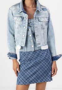 Ljusblå denimjacka med slitna detaljer, ihopparad med en matchande rutig denimminikjol i blå toner och framfickor.