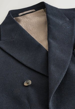 Navy double-breasted jacket with a textured exterior and beige patterned lining. Features wide lapels and a single button closure.