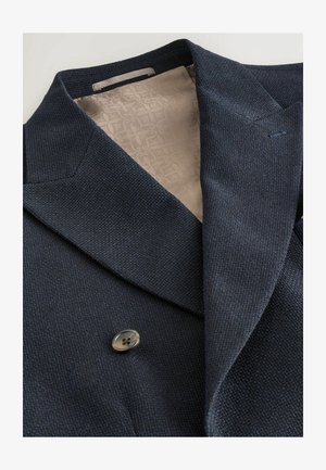 Navy double-breasted jacket with a textured exterior and beige patterned lining. Features wide lapels and a single button closure.