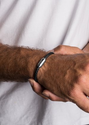 Musta punottu nahkaketju hopeanvärisellä metallisoljella, joka on pukeutunut ranteeseen. Suunnittelussa on teksturoidun pinnan ja tyylikkään siluetin yhdistelmä.