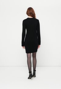 Abito nero in maglia con maniche lunghe, texture a coste e silhouette aderente. Decorato con un collo a girocollo e un sottile motivo a treccia.