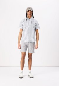 Chemise à rayures bleu clair et blanche à manches courtes, shorts gris, baskets blanches avec accents noirs, et casquette gris clair.