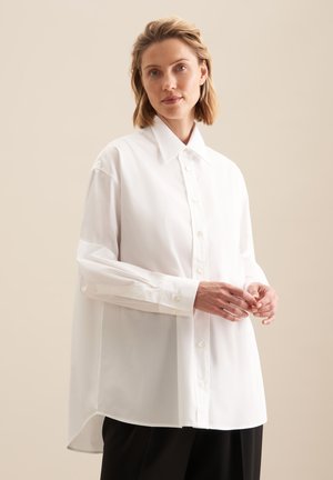 Witte lange mouw button-up shirt met een klassieke kraag, ruim gesneden en gladde textuur, gecombineerd met zwarte broek en een minimalistisch ontwerp.