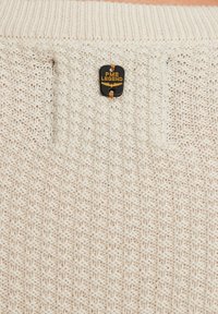 Pull en tricot beige avec un motif texturé, col côtelé et une étiquette PME Legend noire et dorée cousue sur le côté.