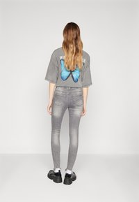 Camiseta gris de gran tamaño con un gráfico de mariposa azul en la parte posterior, combinada con jeans grises ajustados y zapatos negros gruesos. Fondo simple.