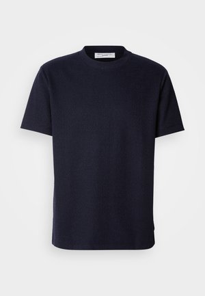 Lyhythihainen, pyöreäkauluksinen t-paita tummansinisestä väristä, valmistettu tekstuurista kankaasta, suoralinjainen leikkaus ja sivuhalkiot liikkumisen helpottamiseksi.