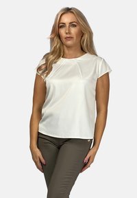 Biała krótko rękawowa bluzka z gładkiego materiału, z okrągłym dekoltem i subtelnym plisowaniem z przodu, w połączeniu z brązowymi spodniami.