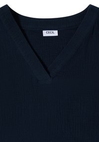Mørk navyblå tekstureret stof top med V-udskæring og en hvid label syet indeni med mærkenavnet "Cecil".