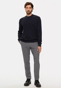 Maglione blu navy a trama con scollo a girocollo, abbinato a pantaloni grigi chiari a motivo e scarpe eleganti nere. Design minimalista.